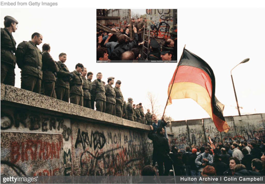 East Germans soldiers standing on Berlin Wall as West Germans begin tearing it down. 