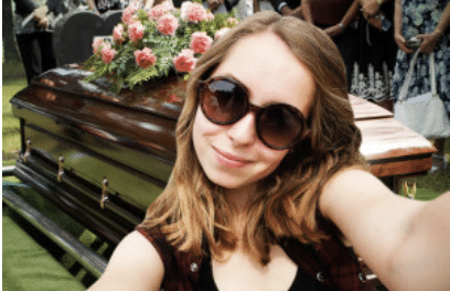 Girl taking selfie in front of casket at funeral