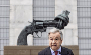 UN Secretary General Antonio Guterres standing in front of iconic statue of pistol with folded muzzle