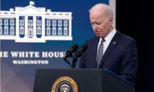 Biden at presidential podium in White House briefing room with head bowed looking sad