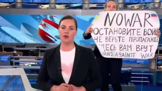 woman runshing on Russian state TV news set and holding up no war protest poster