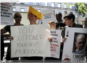 People holding signs mocking Rupert Murdoch at Dominion defamation trial
